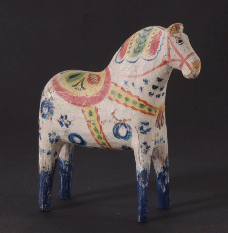 Handsnidad dalahäst i trä med färgglad folklig dekor i rött, blått och grönt mot mörk bakgrund.